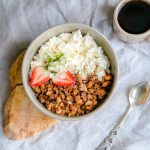 A delicious breakfast bowl with cottage cheese, granola, and strawberries served with black coffee.
