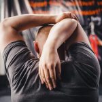 Man stretching arms in a gym, viewed from behind, focusing on fitness and flexibility.